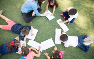 Top view of a group of students and their teacher lying on the grass and learning outdoors