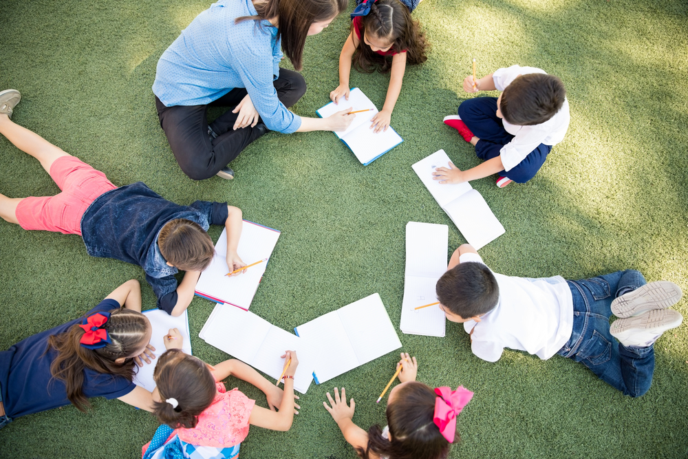 Top view of a group of students and their teacher lying on the grass and learning outdoors