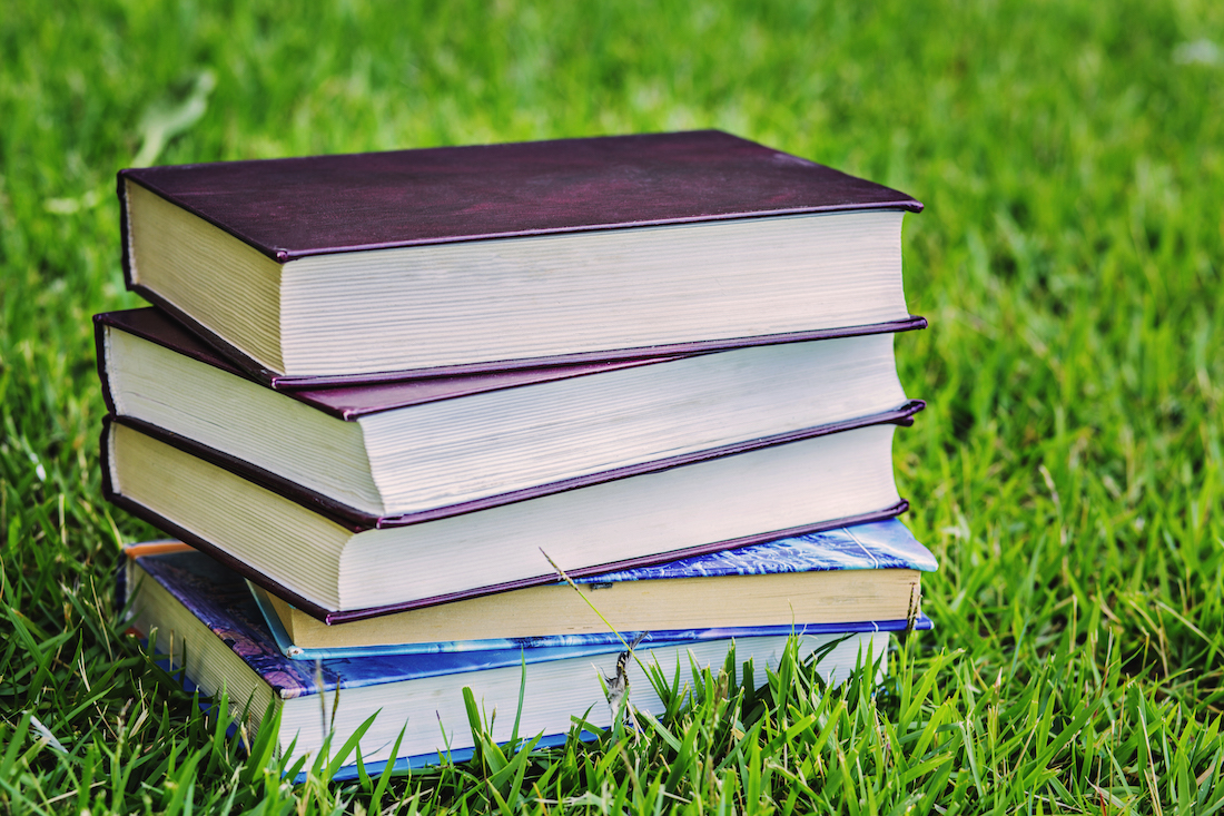 stack of books for summer reading in the grass