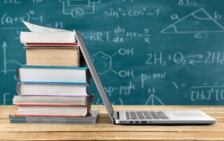 laptop leaning against stack of books with scientific equations in the background