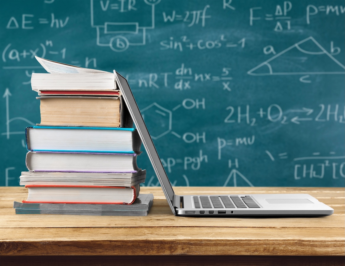 laptop leaning against stack of books with scientific equations in the background