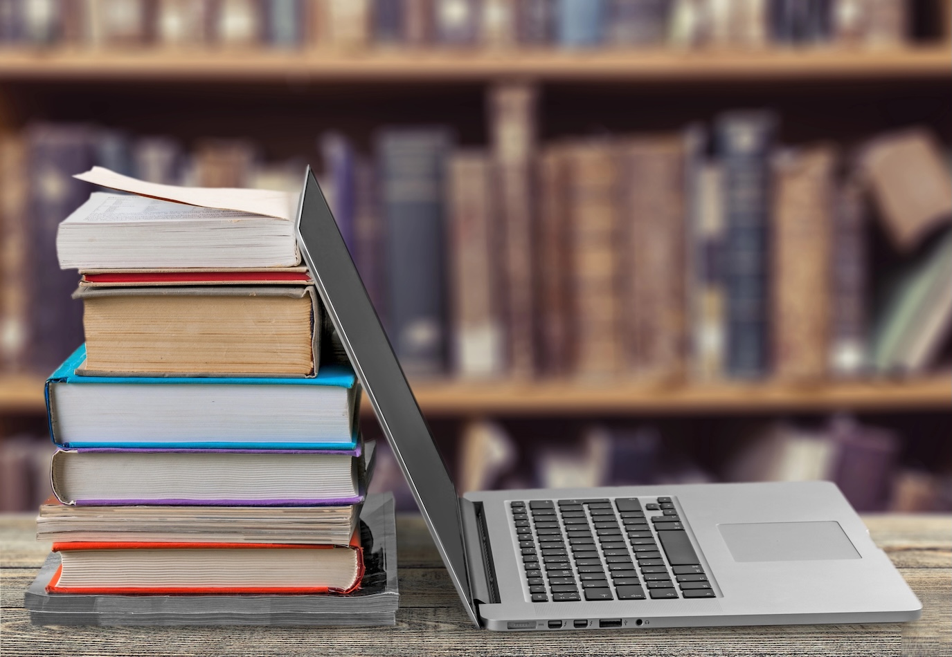 laptop leaning against stack of books in a library for reading and history learning